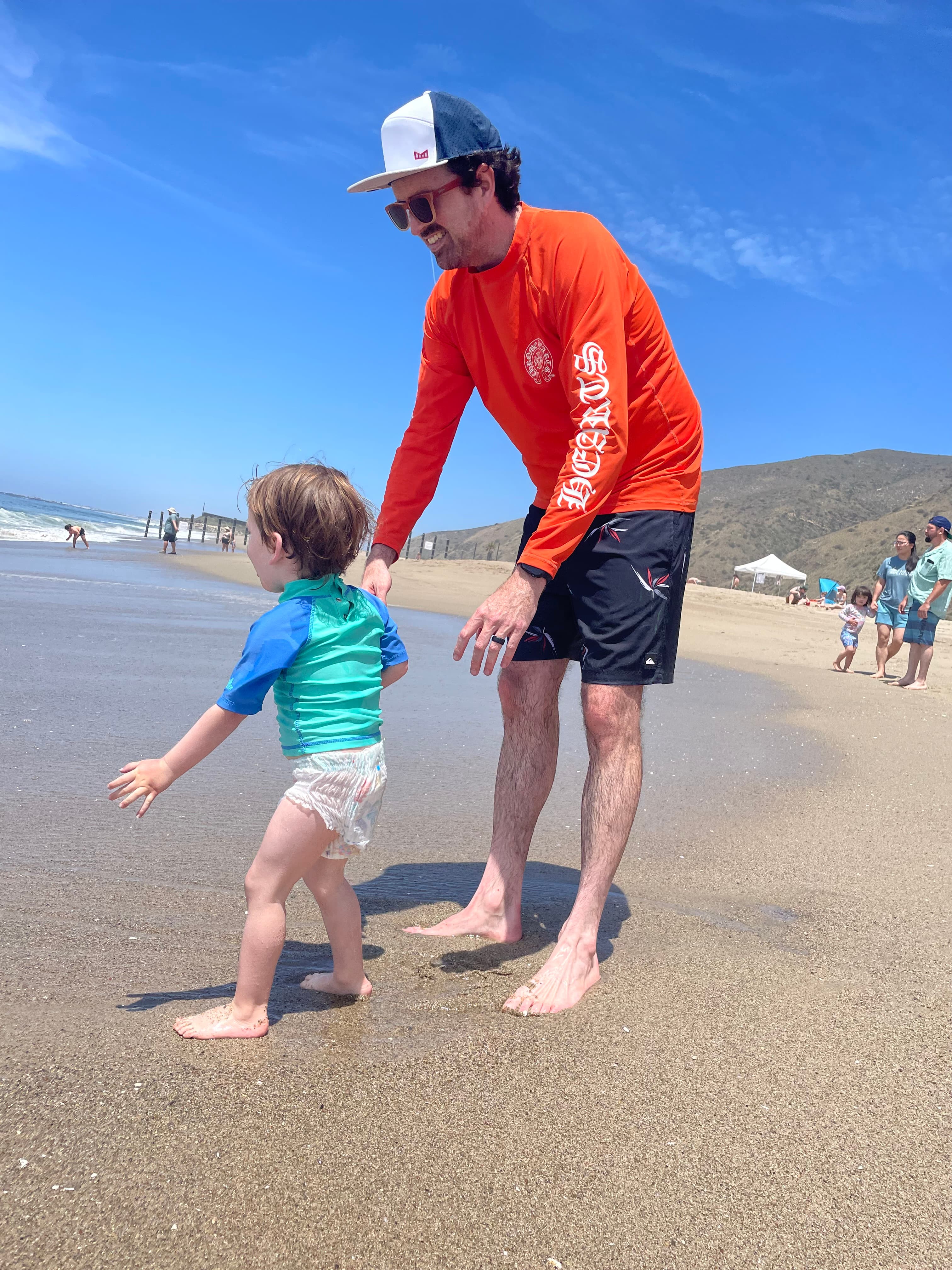 Wide beach scene with adult and child walking toward distant waves